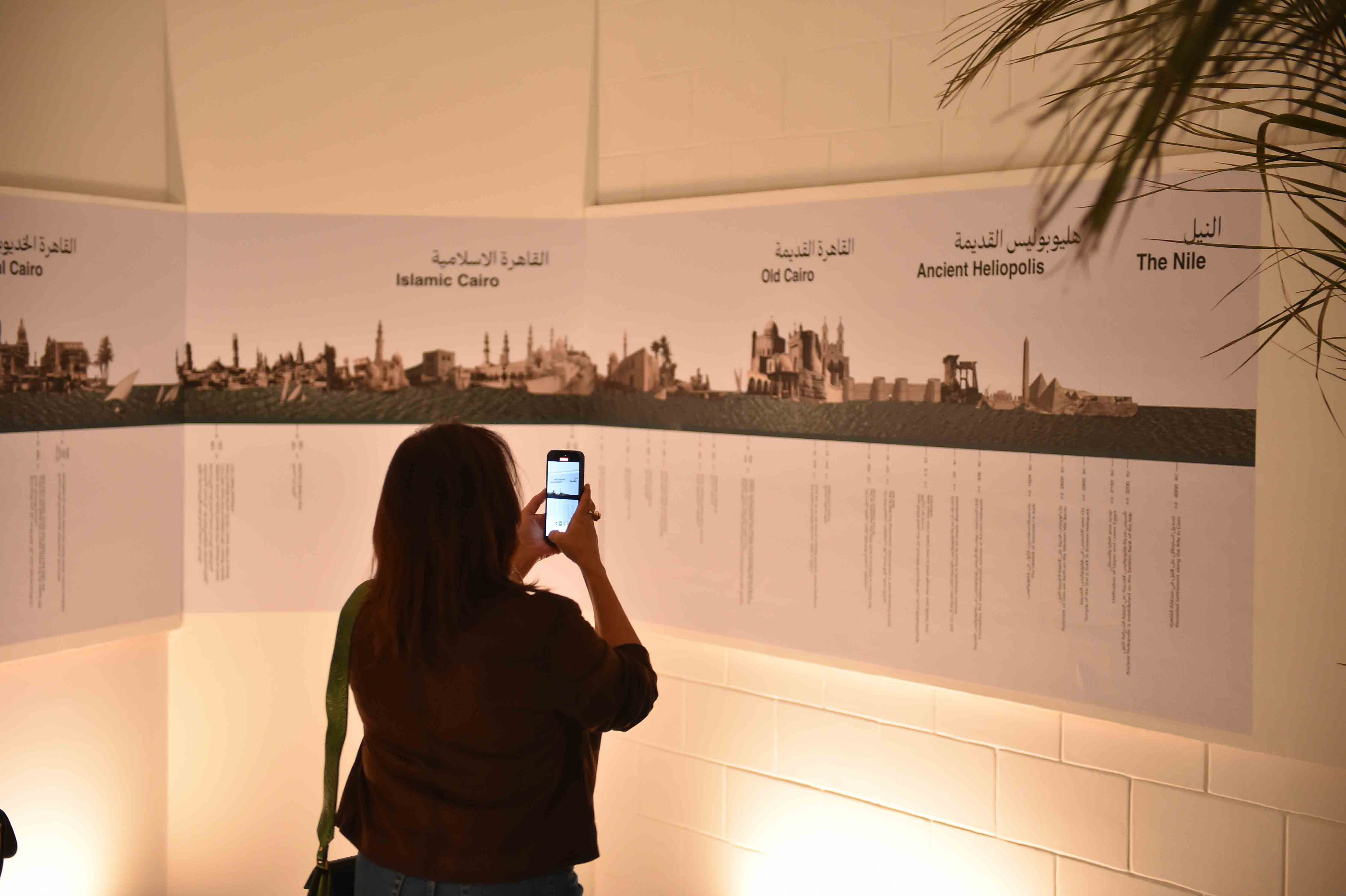 a women holder her mobile taking a picture of a poster in an exhibition room