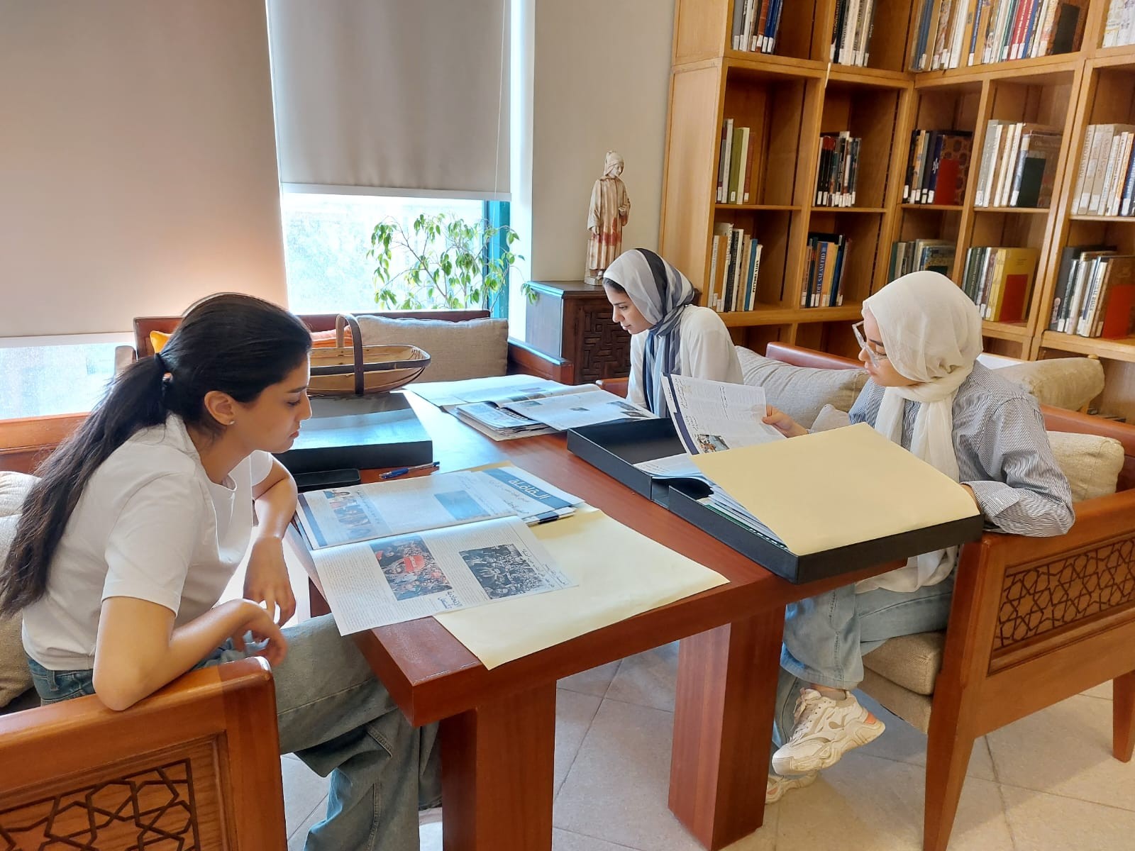 three students viewing magazines in a reading room