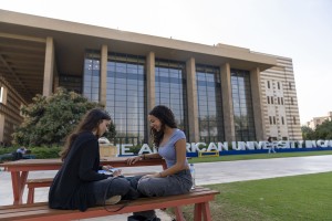 Two girls sitting on a bench infront of AUC Library building